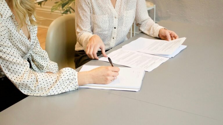 Duas pessoas assinando documentos sobre uma mesa