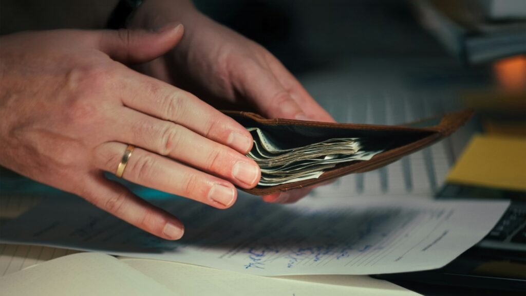 Mãos segurando dinheiro em uma carteira sobre papéis